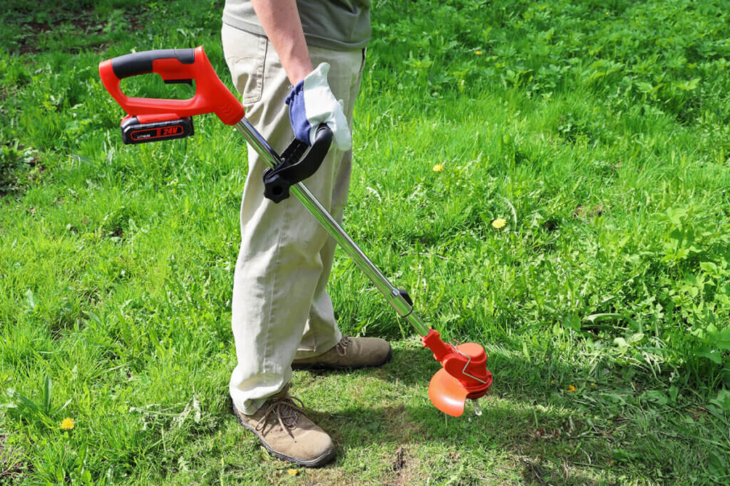 Mann steht mit Rasentrimmer im Garten